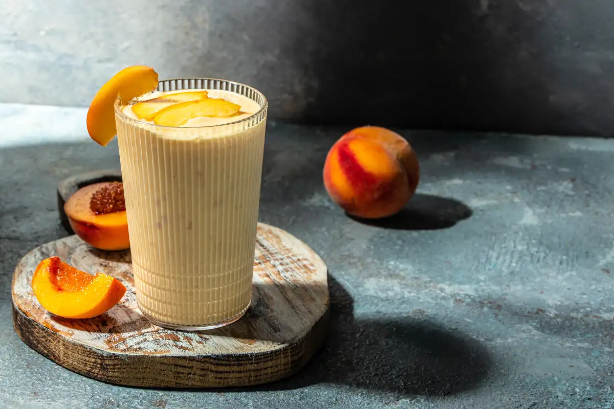 Licuado servido en un vaso de vidrio junto con duraznos