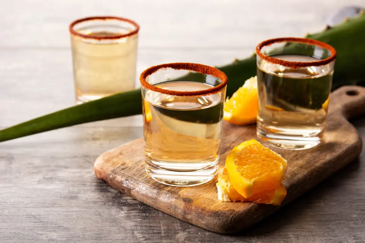 Tabla de madera con caballitos de mezcal acompañados de rodajas de naranja
