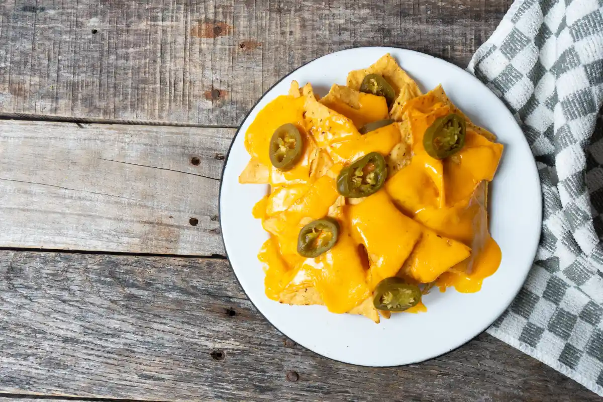En un plato blanco están servidos nachos con queso y jalapeños