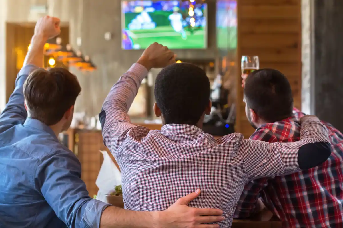 Hombres abrazados viendo una pantalla con un partido de futbol