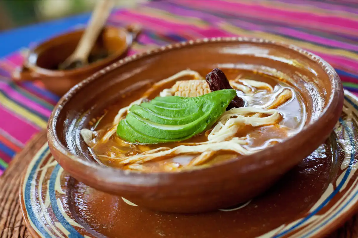 Caldo tlalpeño con aguacate servido en un plato de barro