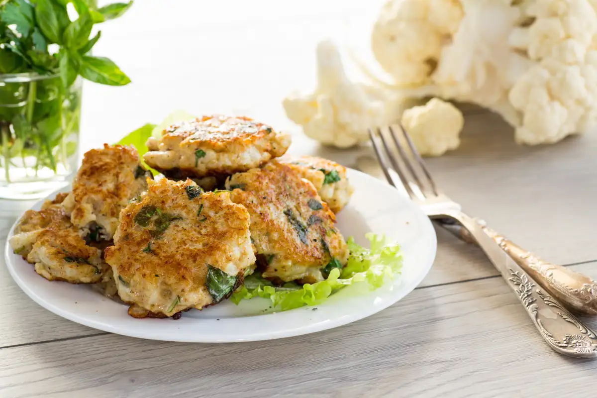 Tortitas de coliflor fritas y vegetarianas cocidas, en un plato sobre una mesa de madera.