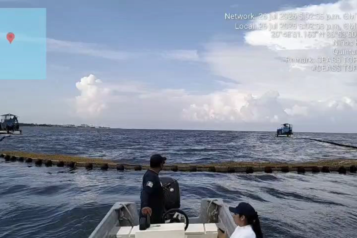 Personal en una embarcación menor supervisando una barrera antisargazo instalada en el mar de Quintana Roo para la contención de algas.