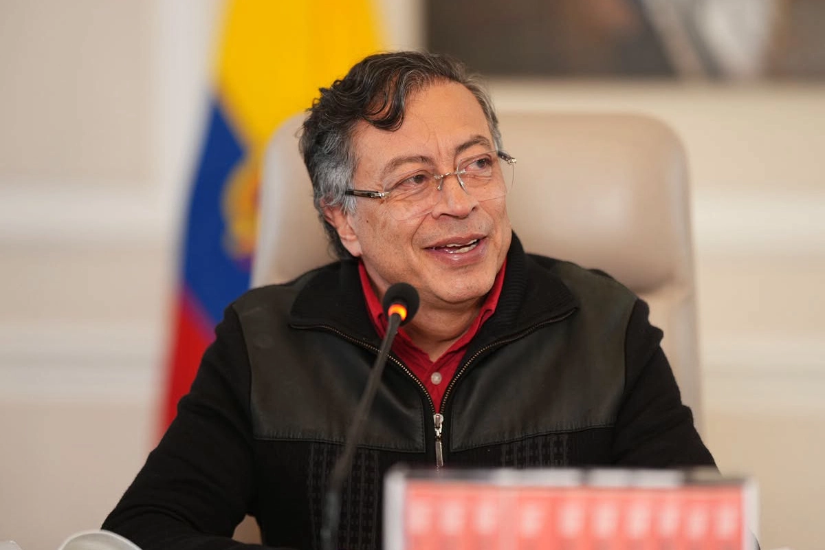 Gustavo Petro sonriendo con una bandera difuminada de Colombia detrás de él