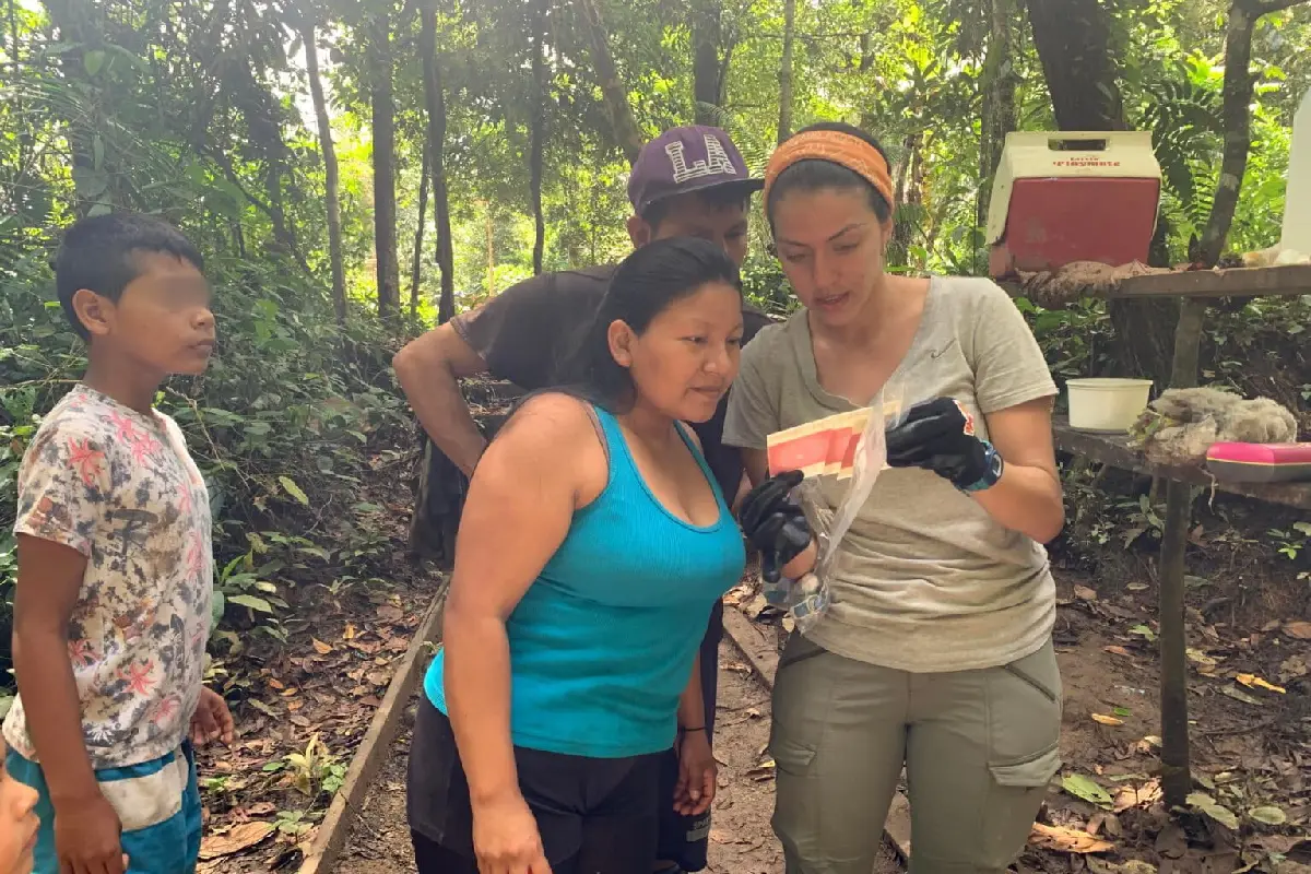 Una investigadora muestra y explica el uso de muestras microbiológicas en placas Petrifilm a una mujer indígena waorani en medio de la selva.