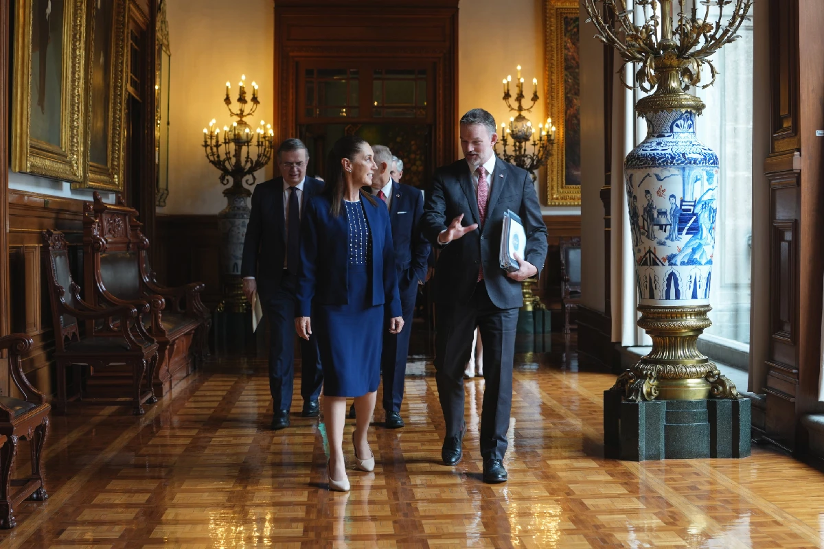 Claudia Sheinbaum y el representante comercial de EE. UU., Jamieson Greer, caminan conversando por un pasillo de Palacio Nacional acompañados por Marcelo Ebrard y su delegación.