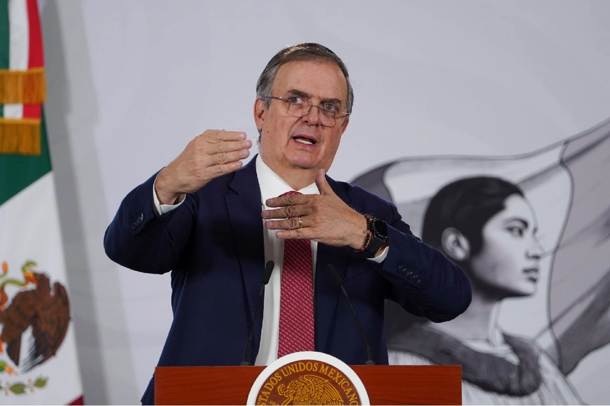 Marcelo Ebrard gesticula con las manos mientras habla frente a los micrófonos desde un pódium oficial con la bandera de México al fondo.