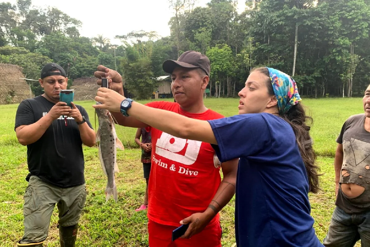 Personas midiendo y pesando un pez en un campo abierto rodeado de vegetación.