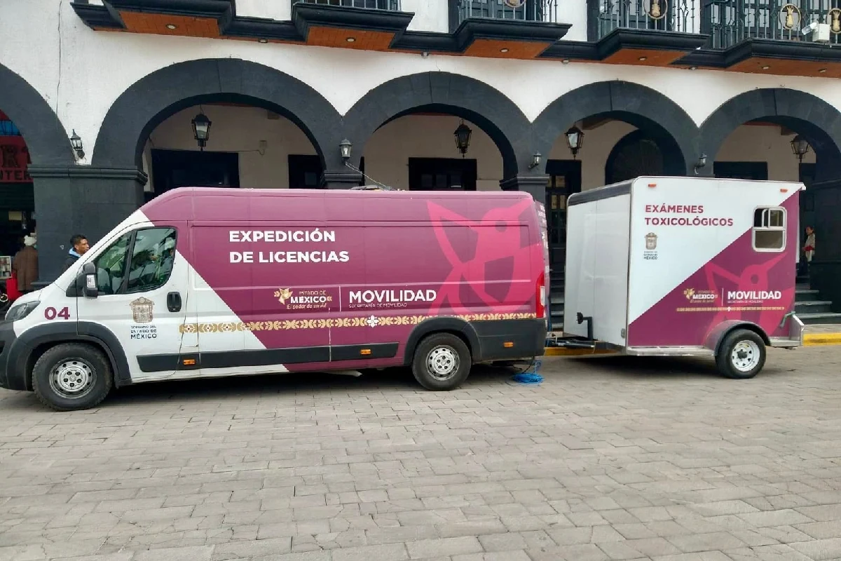 Camioneta de la Secretaría de Movilidad del Estado de México para expedición de licencias con un remolque adjunto para exámenes toxicológicos, estacionada frente a portales arquitectónicos.