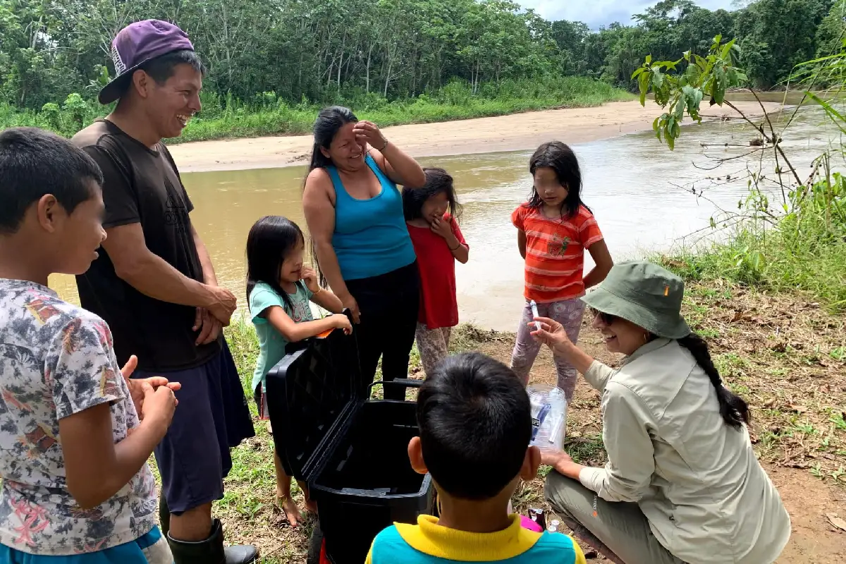 Una investigadora muestra instrumental científico a una familia indígena a orillas de un río en la selva.