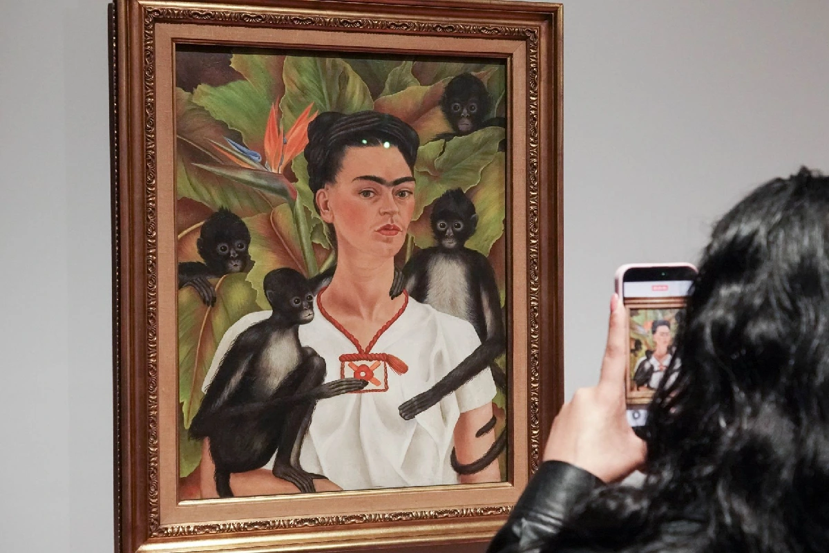 Retrato de Frida Kahlo siendo fotografiada por una persona de cabello largo con su celualr