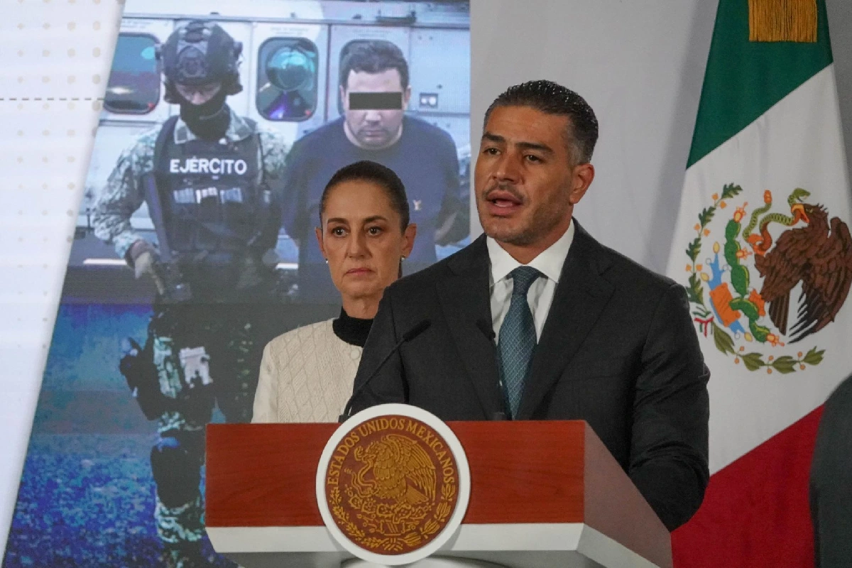 Omar García Harfuch habla desde el podio en conferencia de prensa junto a la presidenta Claudia Sheinbaum, con una pantalla al fondo mostrando a un detenido resguardado por el Ejército.