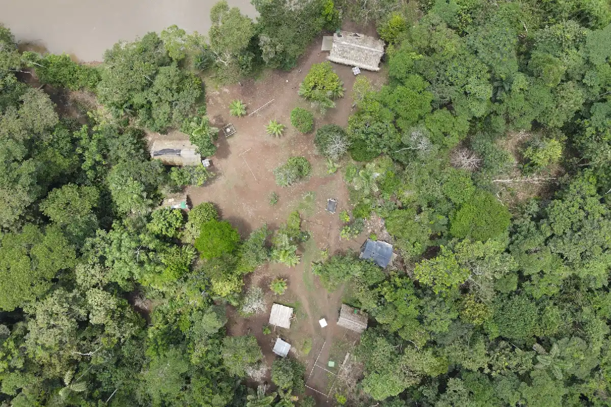 Vista aérea de una aldea con cabañas tradicionales rodeada por la frondosa vegetación de la selva amazónica.