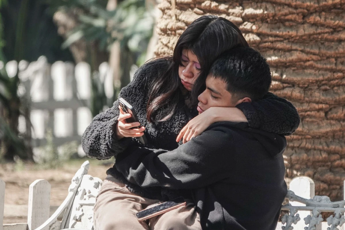 Una mujer sentada en las piernas de un hombre ambos viendo un celular 