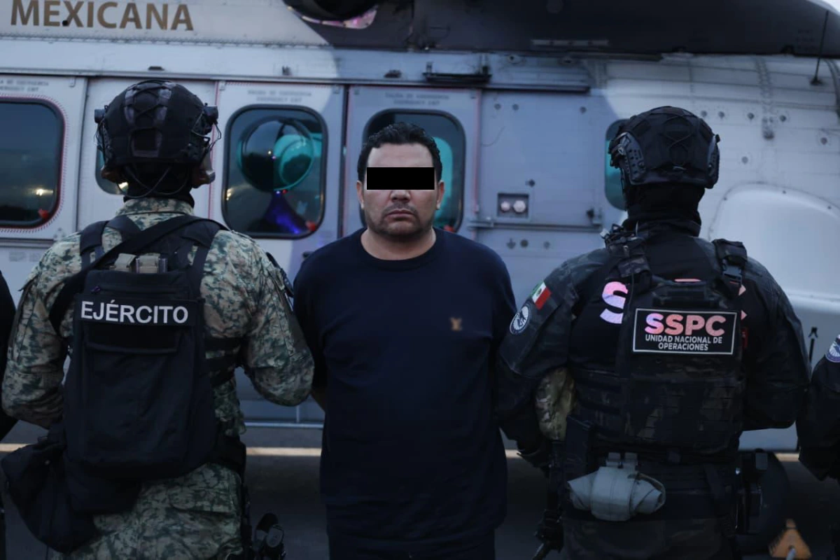 Hombre detenido con el rostro censurado por una barra negra, custodiado por dos agentes federales de uniforme táctico del Ejército y de la SSPC, frente a un helicóptero oficial.
