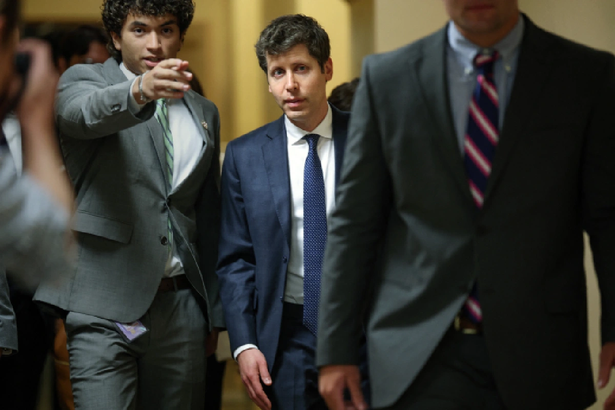 Sam Altman, CEO de OpenAI, caminando en traje azul y corbata rodeado de asesores y fotógrafos por los pasillos del Congreso de EE. UU.