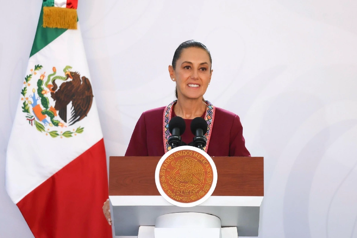 Sheinbaum en conferencia de prensa desde Michoacán con la bandera de México atrás y vestimaenta lila