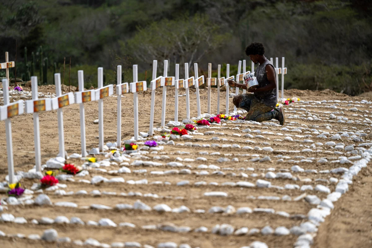 Un hombre arrodillado coloca flores en una fila de tumbas con cruces blancas tras los terremotos en Venezuela.
