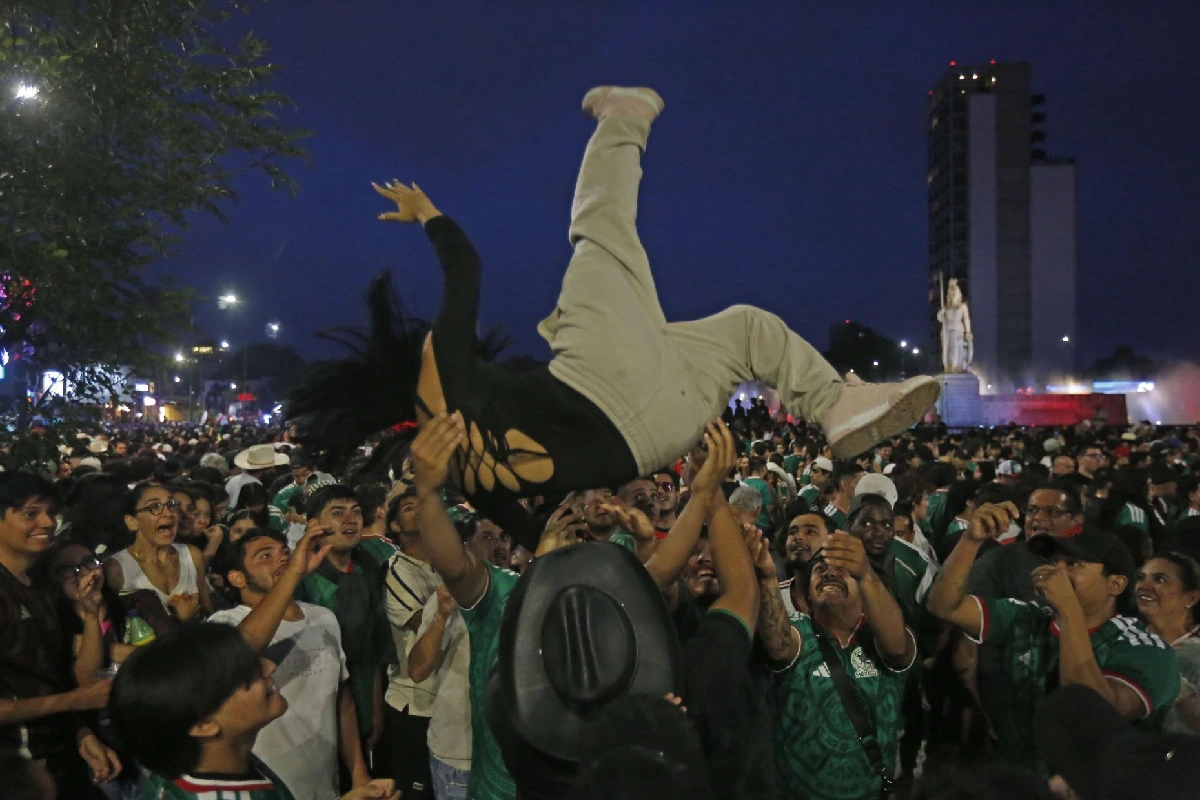 Aficionada con blusa negra volando tras ser lanzada por aficionados de México que esperan a atraparla
