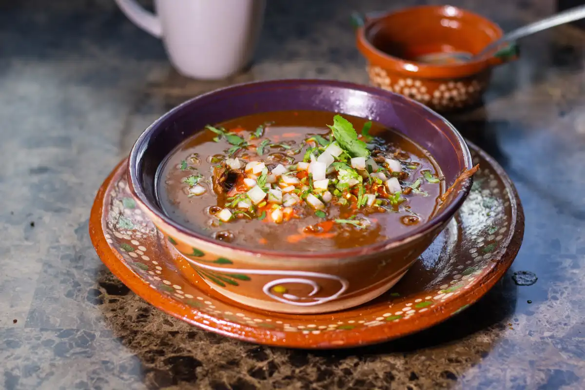 Plato de barro con caldo de birria de res