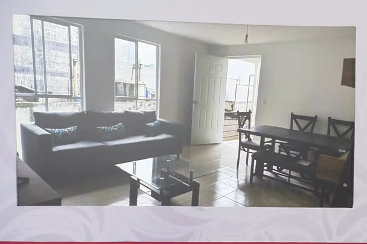 Sala de un departamento con un sillón negro pegado a la puerta y a una ventana y un comedor en medio de la escena