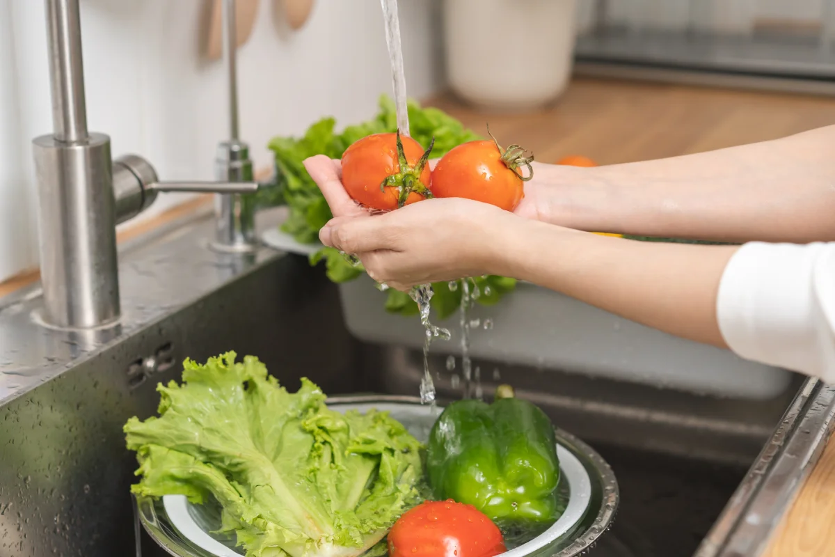 Cerca de tomate, mujer joven asiática lavando brócoli, zanahoria, verduras frescas, pimentón con agua salpicada en un recipiente de agua en el fregadero en la cocina, preparando ensalada fresca, comida para cocinar. 