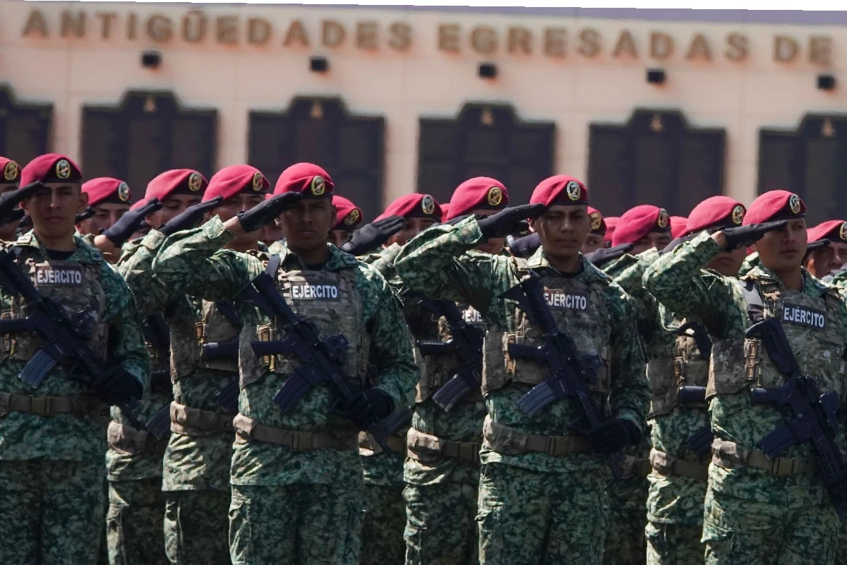 Grupo de militares portando gorras boinas rojas, equipo táctico y armas de fuego, realizando el saludo militar en formación.