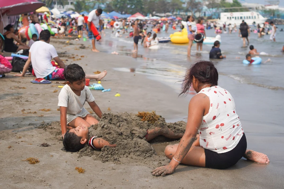 Un grupo de niños entierra a otro en la arena como parte de un juego a la orilla de la playa 