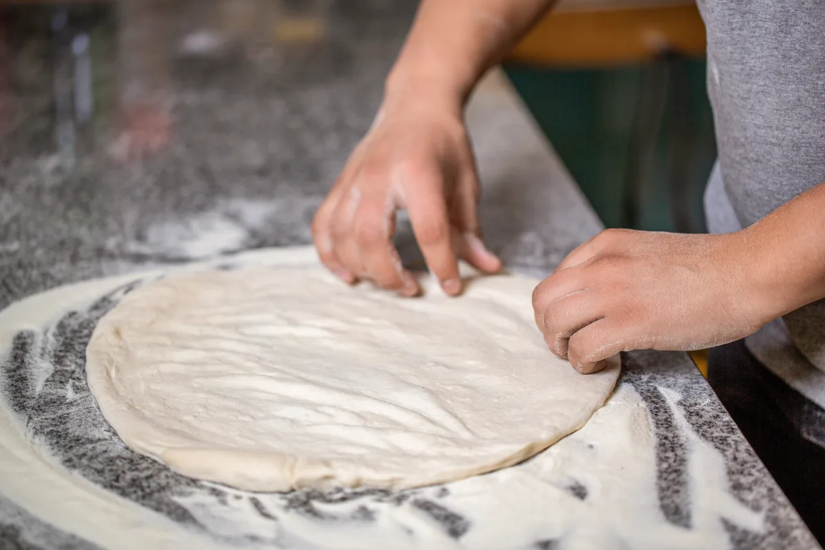 Persona comienza a darle forma circular a la masa para pizza