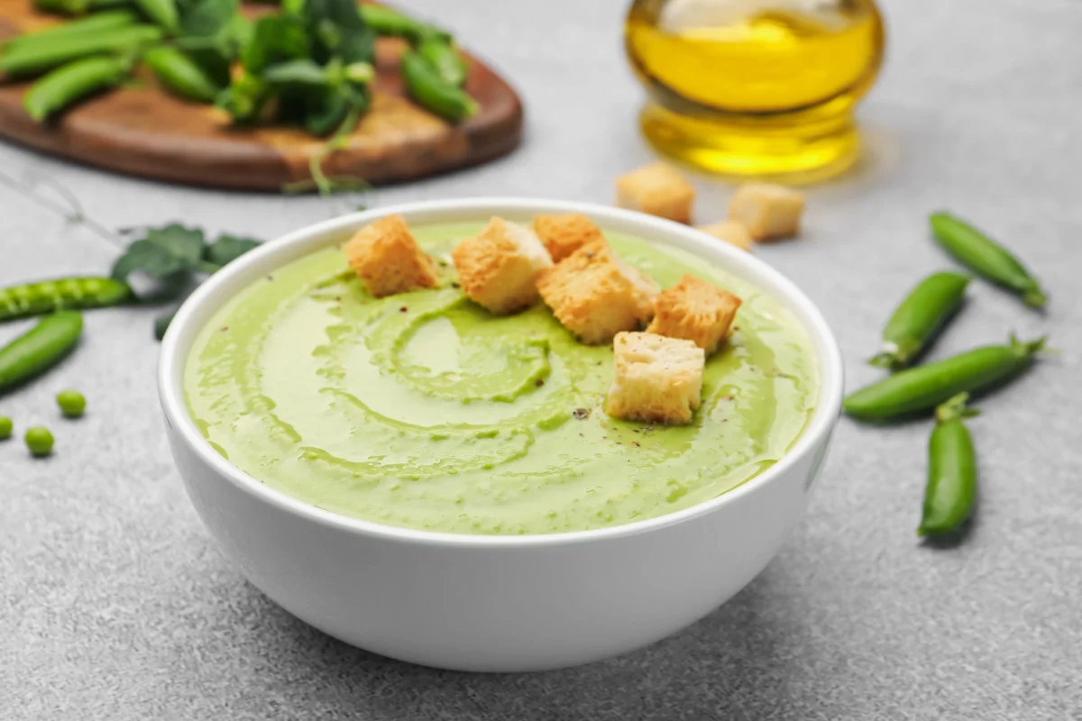 Sabrosa sopa de crema de guisantes con crutones servidos en la mesa gris, en primer plano.