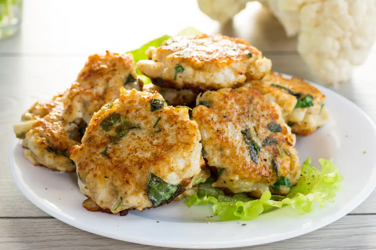 Tortitas de coliflor fritas y vegetarianas cocidas, en un plato sobre una mesa de madera.