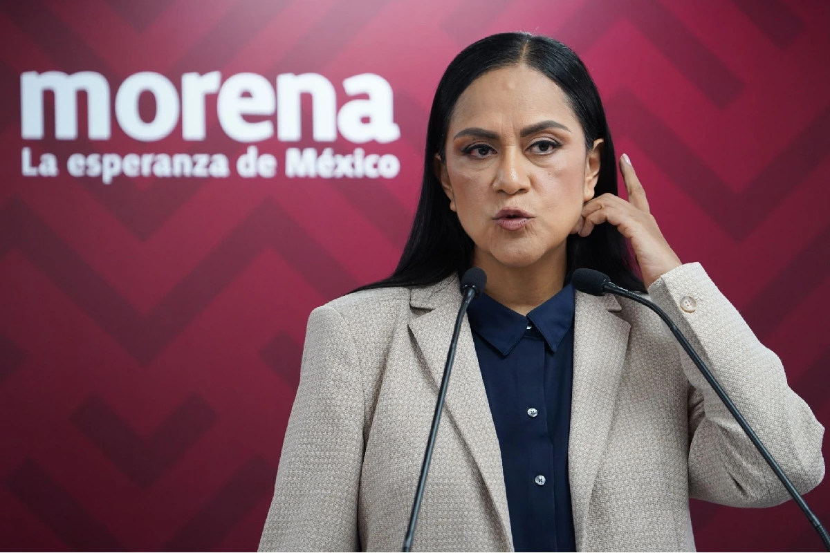 Ariadna Montiel Reyes acomodándose el cabello mientras habla en un podio frente al logotipo del partido Morena.