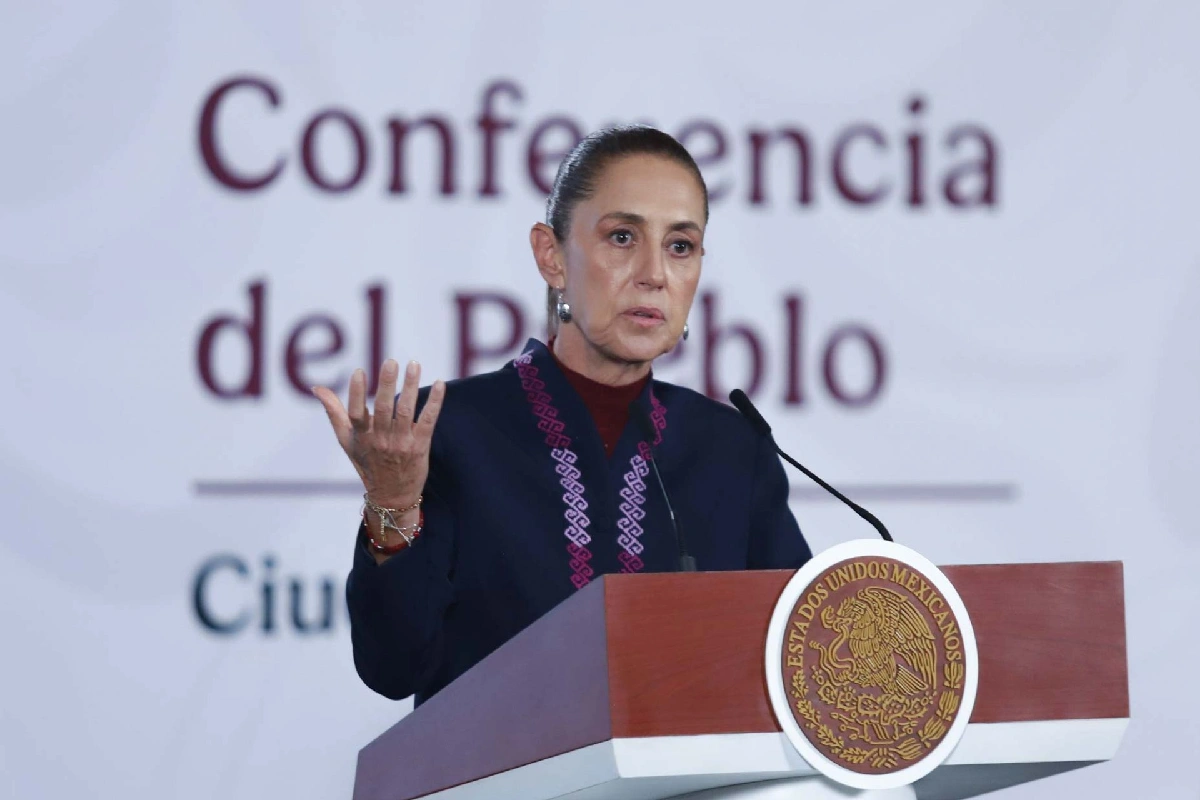 La presidenta Claudia Sheinbaum gesticulando con la mano derecha desde el pódium presidencial con el fondo de "Conferencia del Pueblo".