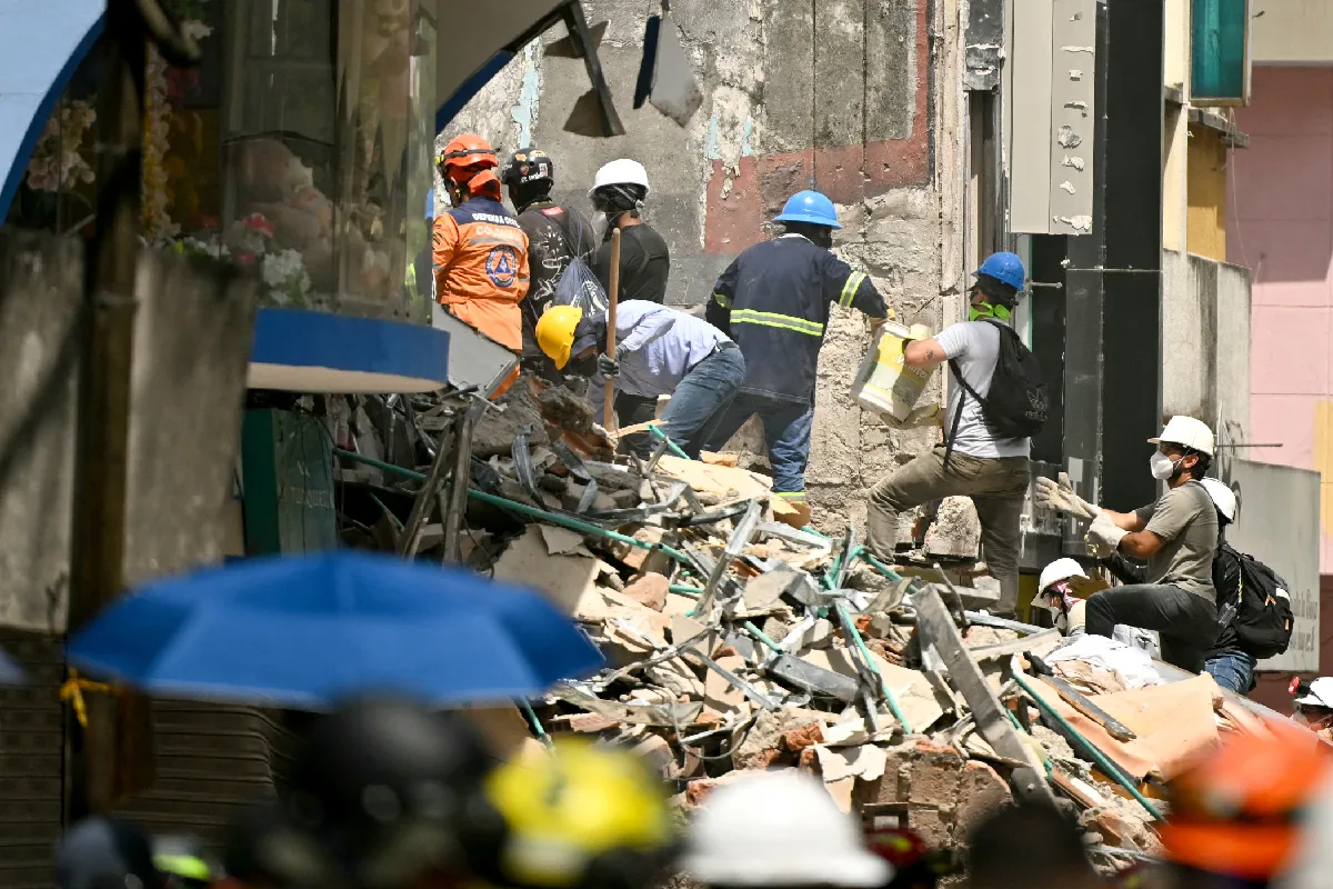 Varios rescatistas y voluntarios con cascos de protección remueven escombros y restos de concreto de un edificio colapsado tras un terremoto.
