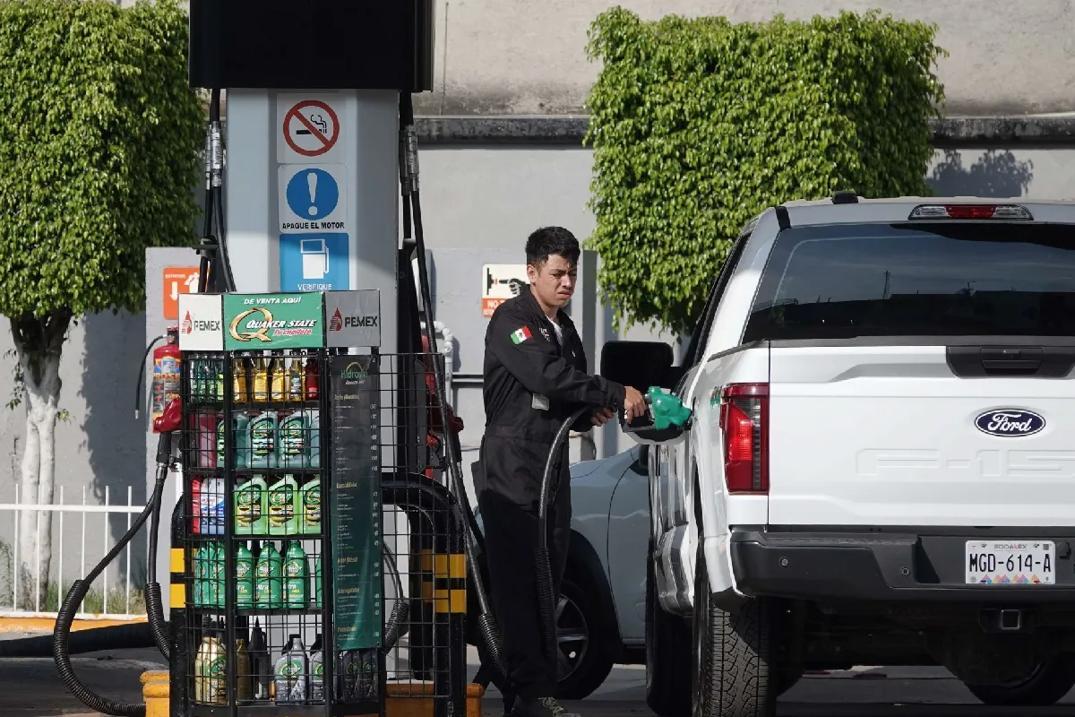 Despachador de combustible vistiendo uniforme negro cargando gasolina a una camioneta blanca Ford F-150 en una estación de Pemex.