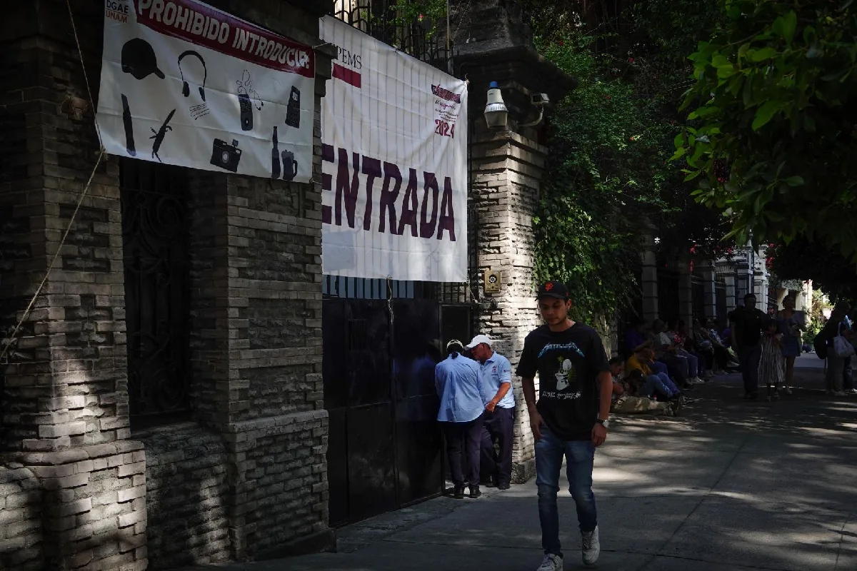 Un joven pasando frente a una escuela con una lona que dice entrada