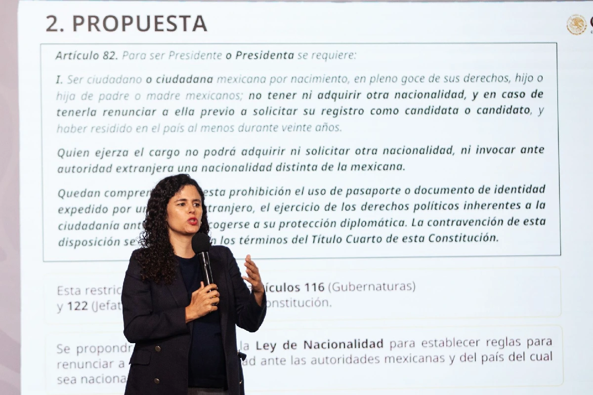 Luisa María Alcalde exponiendo con un micrófono frente a una pantalla institucional con la propuesta de reforma al Artículo 82 constitucional sobre la restricción de doble nacionalidad para cargos públicos.