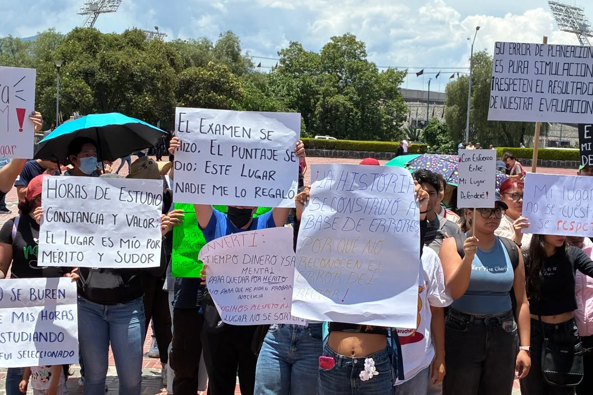 Estudiantes y aspirantes se manifiestan en la vía pública sosteniendo pancartas de protesta con exigencias por sus resultados de examen de admisión educativa.