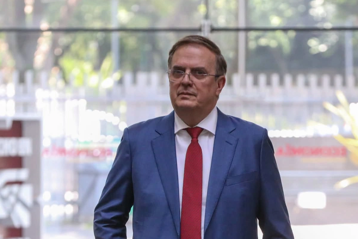 Marcelo Ebrard de traje azul con corbata roja caminando. 