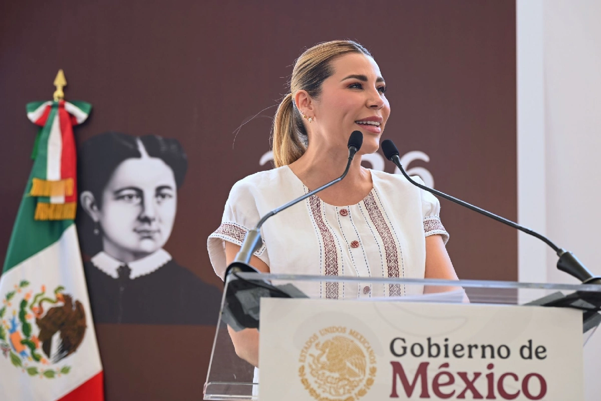 La gobernadora Marina del Pilar Olmeda hablando en un pódium con el logotipo del Gobierno de México, vistiendo un blusa blanca con bordados artesanales, con la bandera de México al fondo.