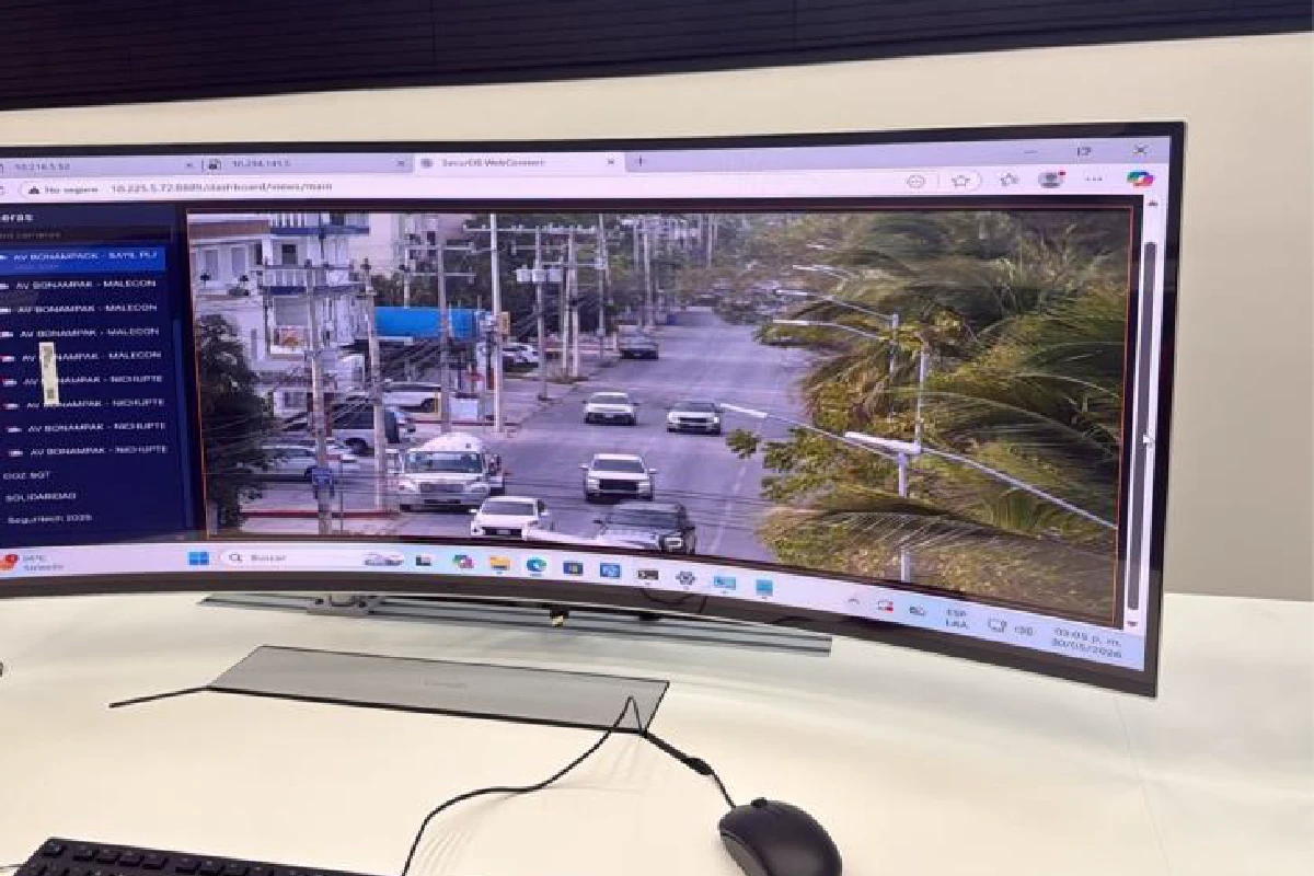 Monitor curvo en un centro de control mostrando la transmisión en vivo de una cámara de videovigilancia enfocada en una avenida con tráfico vehicular y palmeras.