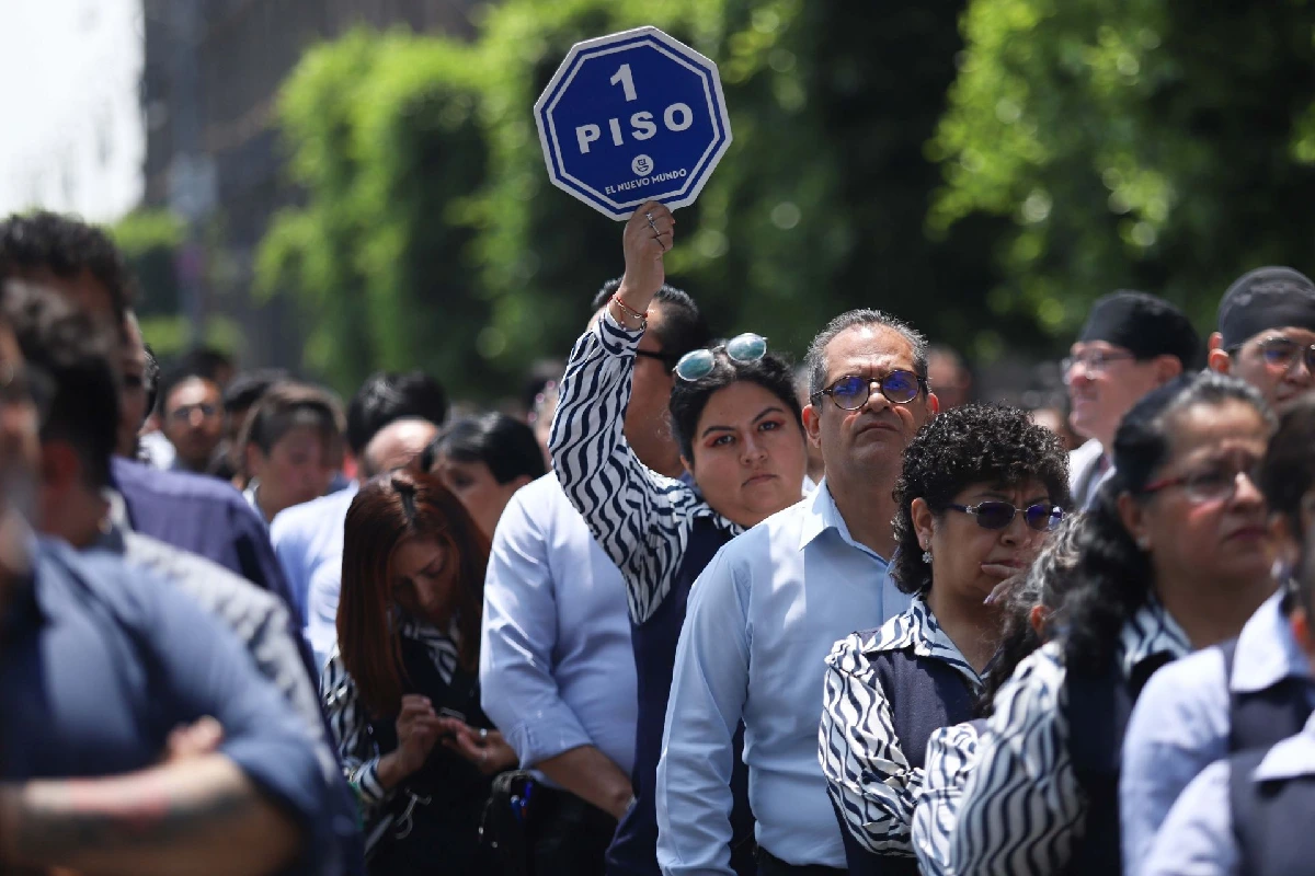 Grupo de personas reunidas en la vía pública durante una evacuación, con una mujer sosteniendo en alto una paleta octagonal azul con la leyenda "1 PISO".