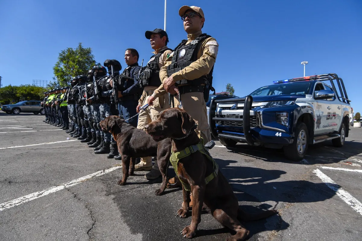 Policías en fila con binomios caninos y una patrulla detra´s de ellos 