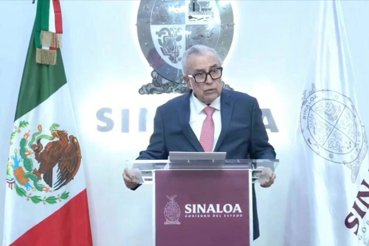 Rubén Rocha Moya, gobernador de Sinaloa, de traje oscuro y corbata rosa, hablando desde el pódium institucional entre la bandera de México y la del estado.