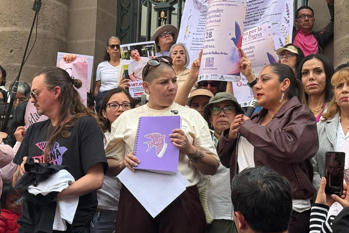 Samara Martínez junto a un grupo de manifestantes sosteniendo una libreta morada con la silueta de un ave, carteles y micrófonos durante una protesta por el derecho a una muerte digna en la Ciudad de México.