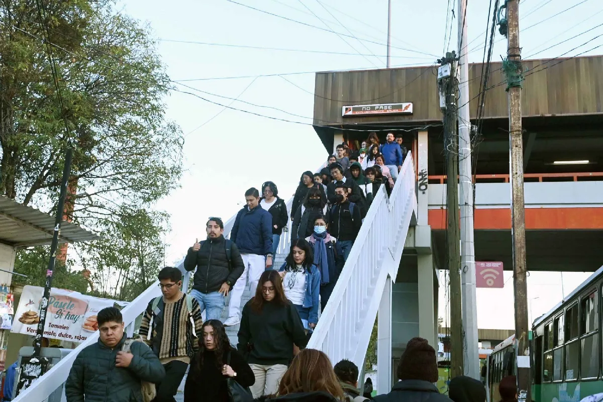 Grupo numeroso de estudiantes bajando por las escaleras de acceso a un puente peatonal y estación del Pumasbús en Ciudad Universitaria de la UNAM.