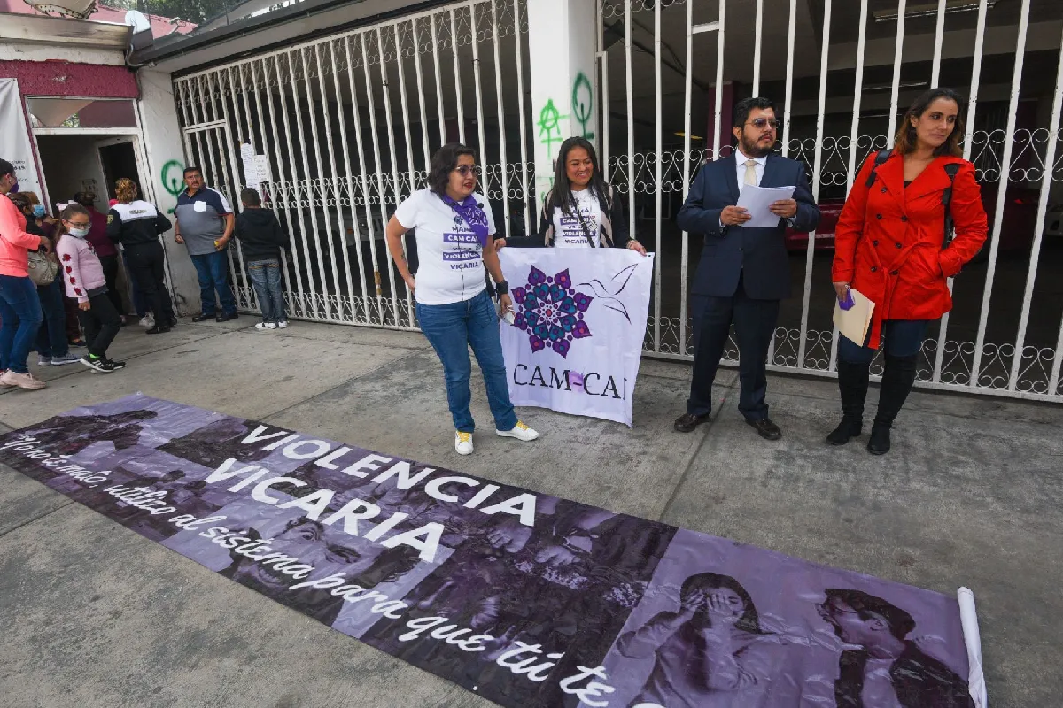 Integrantes de la colectiva CAM-CAI en México sostienen una manta frente a una reja metálica durante una protesta pacífica contra la violencia vicaria.