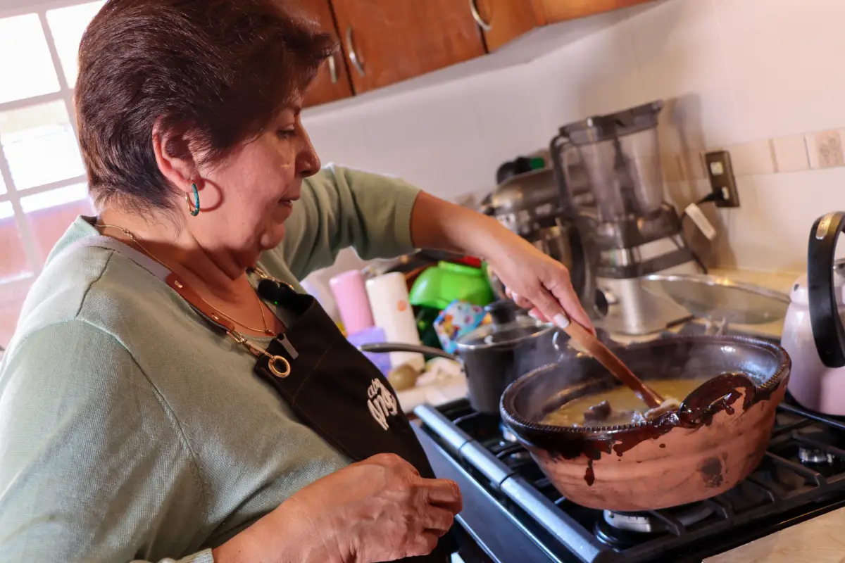 Mujer adulta cocinando en una olla de barro al interior de una cocina mexicana