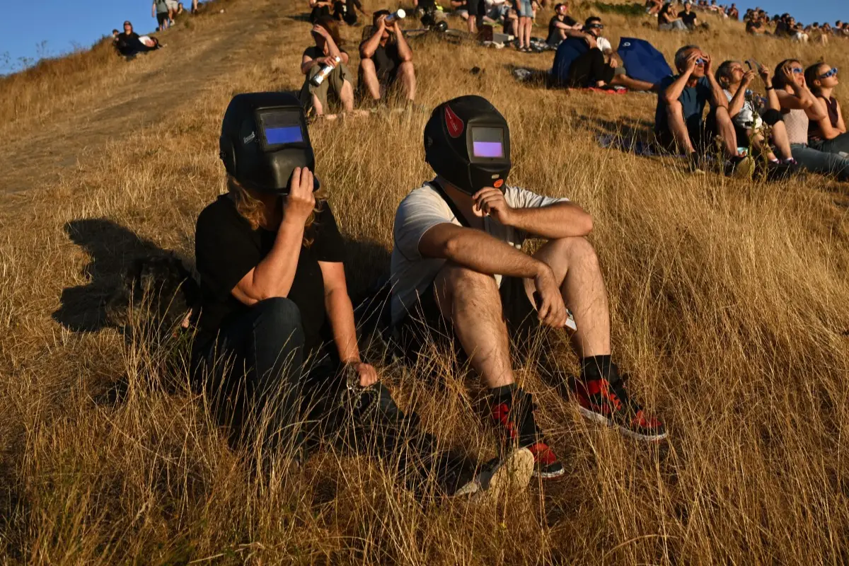 Personas observan a través de pantallas de soldadura el eclipse solar