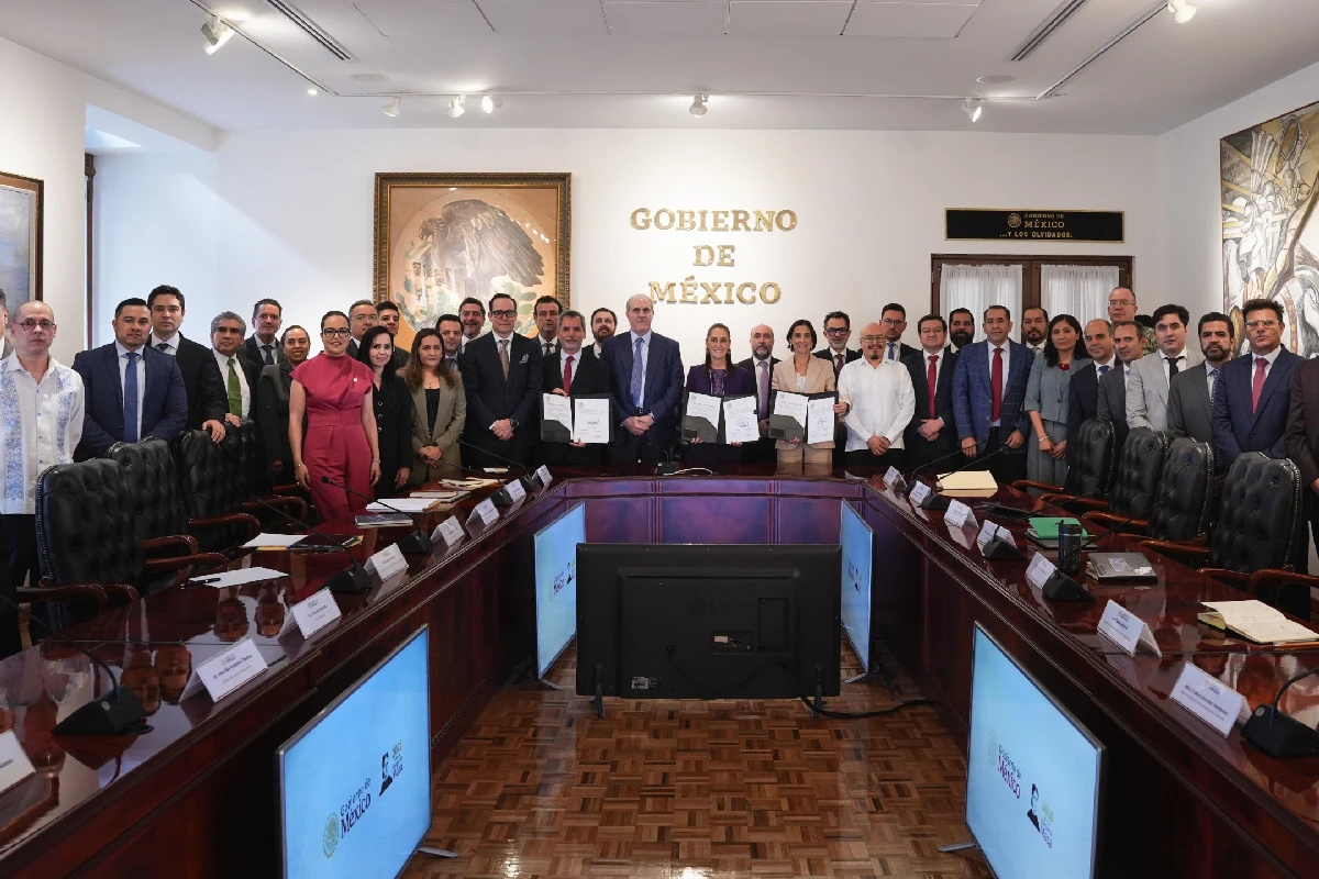 Claudia Sheinbaum y funcionarios de gobierno junto a empresarios gasolineros mostrando los documentos firmados del acuerdo de precios alrededor de una mesa de reuniones.